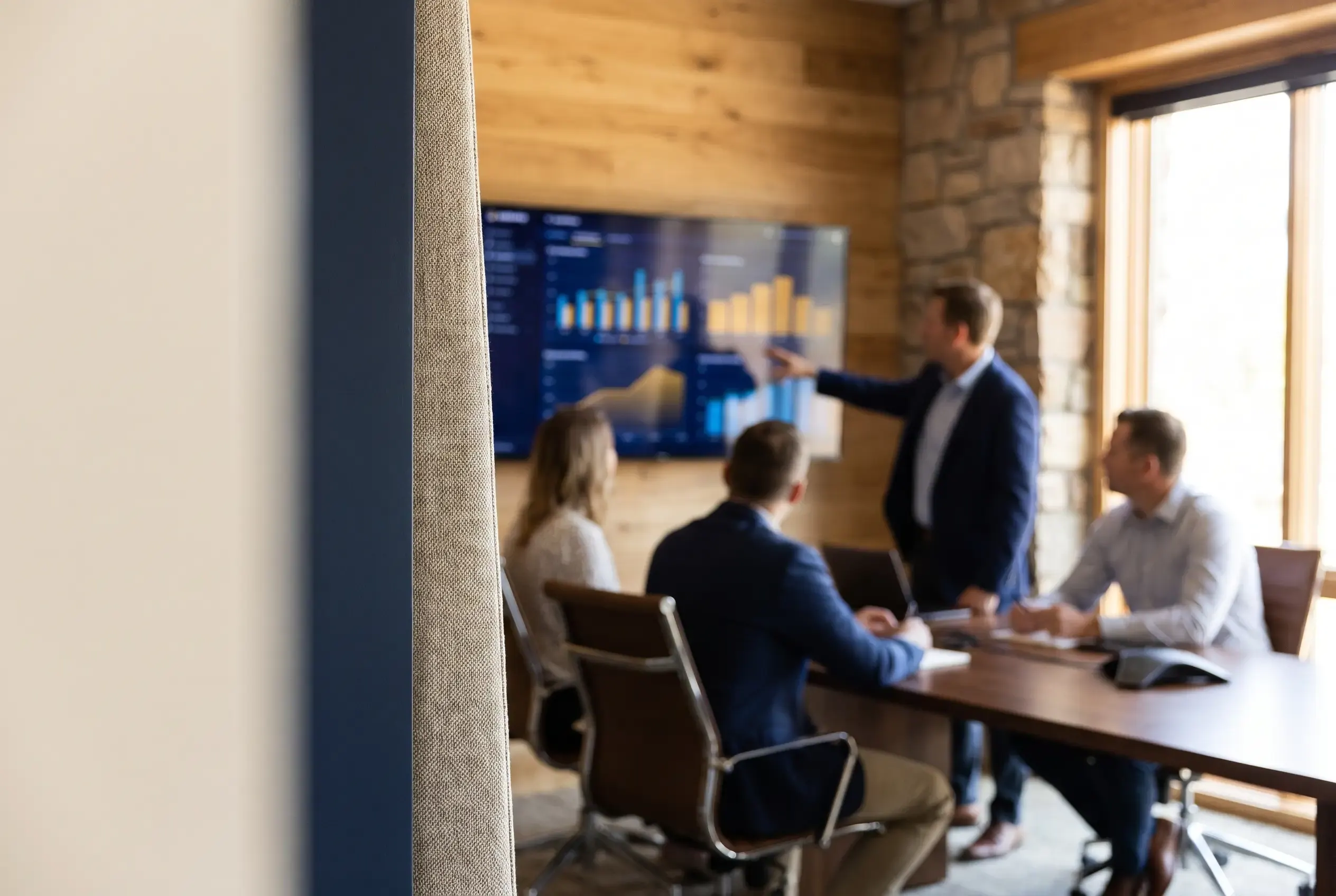 A small team around a table reviewing a dashboard on a wall screen